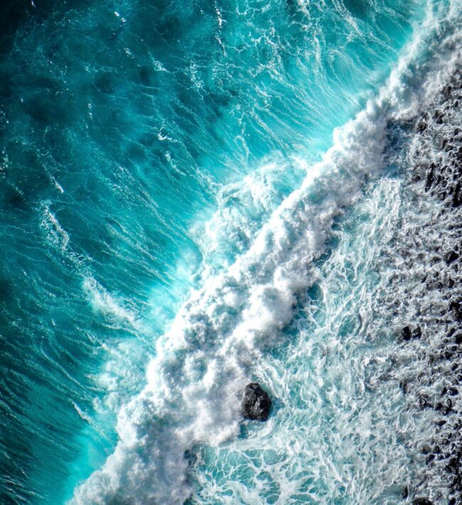 An image of waves crashing on the shore from above